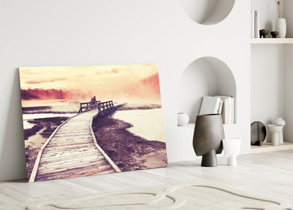 Canvas print leaning against white wall showing wooden boardwalk extending toward misty lake and forest at sunset.