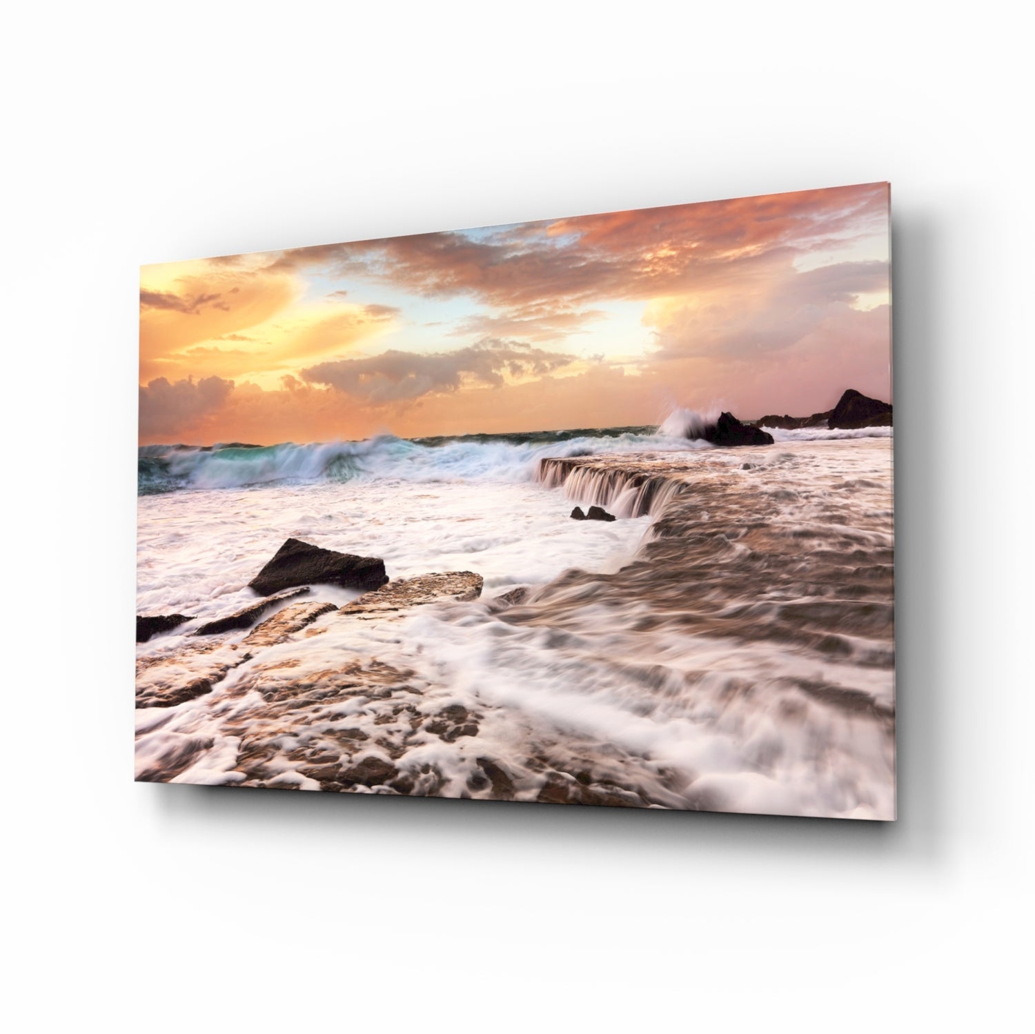 Coastal sunset scene with rolling waves, rocky shore, and golden-orange sky displayed on tilted glass wall art panel.