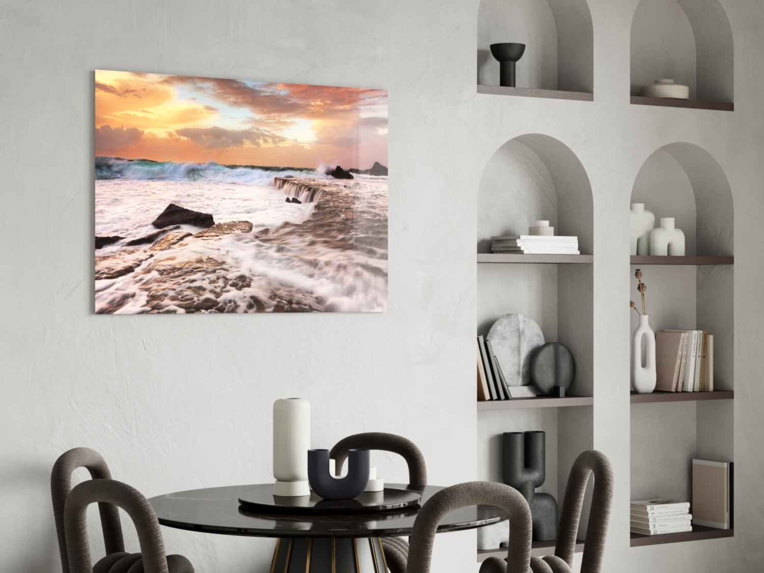 Coastal sunset glass wall art depicting rocky beach with golden sky and waves, displayed above dining table in modern interior.