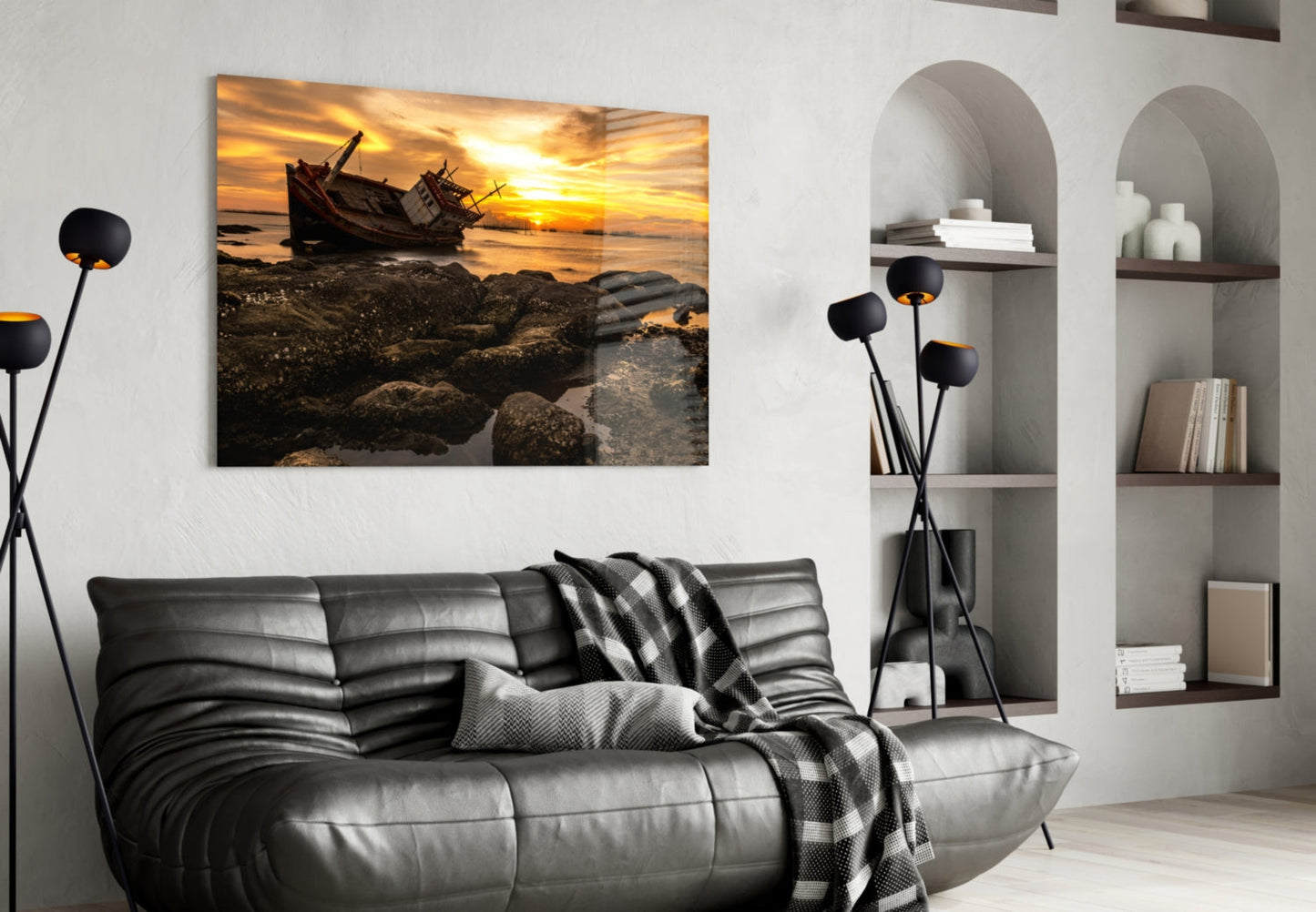 Shipwreck glass wall art displaying a golden sunset with beached boat and rocky shore, hung above a gray leather sofa in a modern living room.