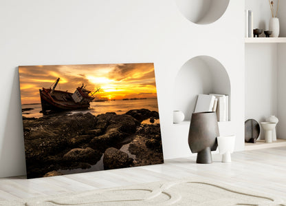 Shipwreck glass wall art leaning against white wall displays golden sunset over abandoned boat and rocky shore.