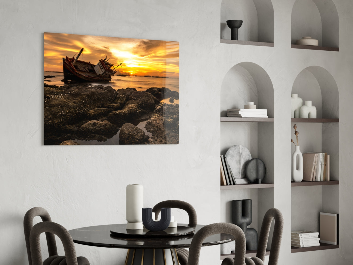 Shipwreck glass wall art depicting an abandoned wooden boat at sunset on rocky shore, displayed above a dining table in a modern interior.