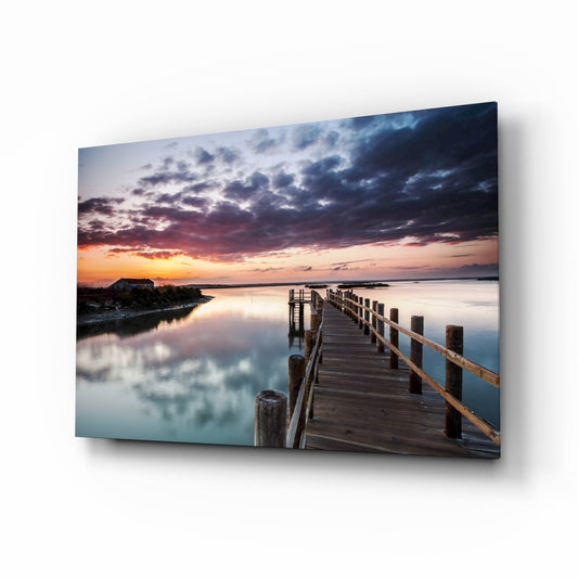 Wooden jetty extending into calm water at sunset with dramatic cloudy sky reflected below, displayed as glass wall art.