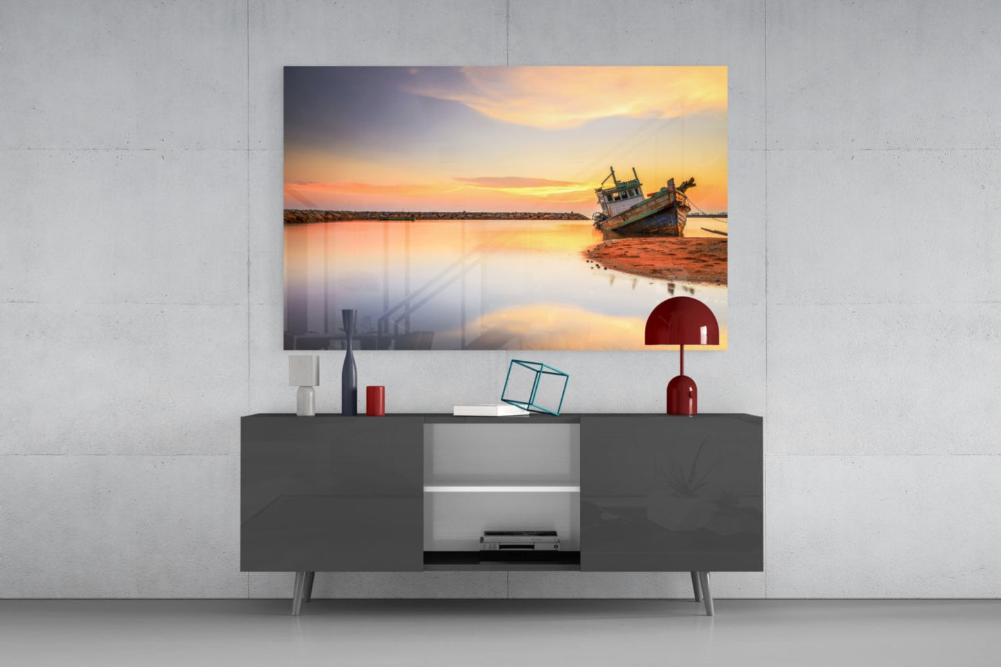 Glass wall art print of a fishing boat at sunset displayed above a dark gray media console in a modern living room setting.