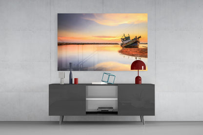 Glass wall art print of a fishing boat at sunset displayed above a dark gray media console in a modern living room setting.