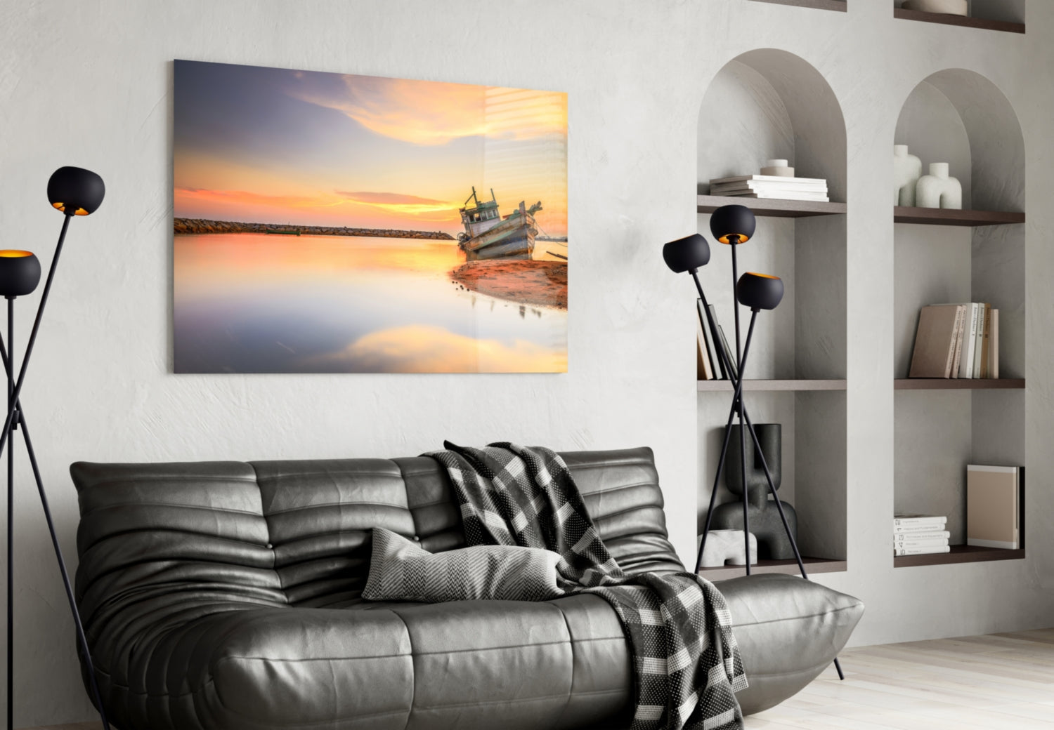 Glass wall art depicting a wooden fishing boat at sunset with golden sky and calm water, displayed above a black leather sofa in a modern living room.