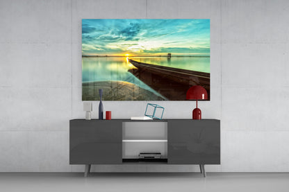 Glass wall art depicting a wooden kayak on beach at golden sunset displayed above a dark media console in modern living room setting.