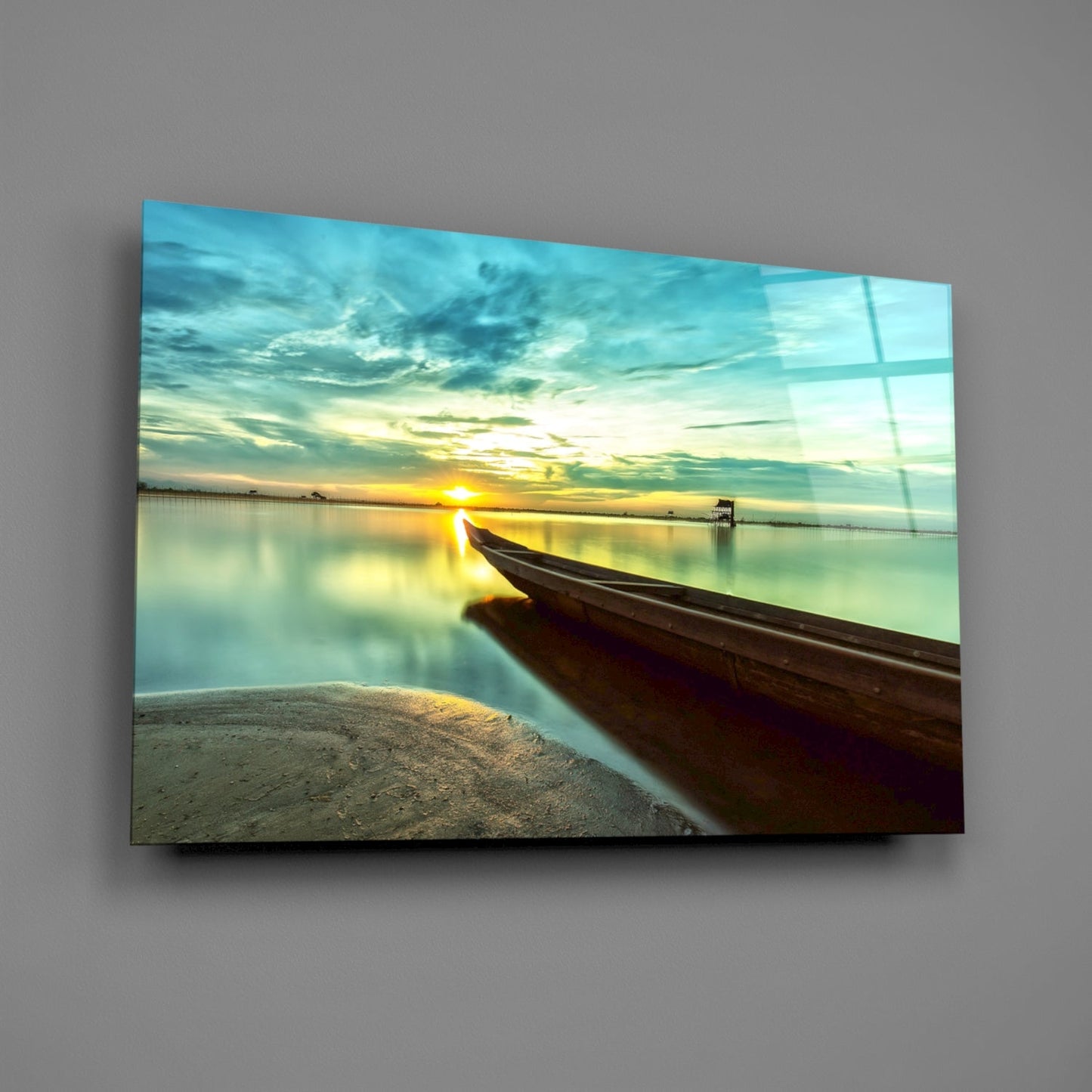Glass wall art depicting a wooden boat on sandy beach at sunrise, with calm turquoise water and golden sky reflected on glossy surface.