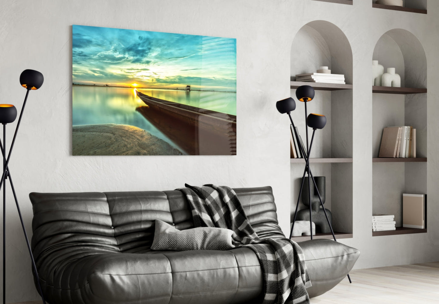 Glass wall art depicting a wooden kayak beached at sunset by calm turquoise water, displayed above a black leather sofa in a modern living room.