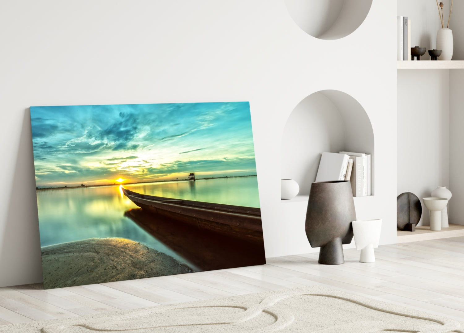 Glass wall art leaning against white wall displays dark wooden kayak on beach with turquoise sunset water and sky.