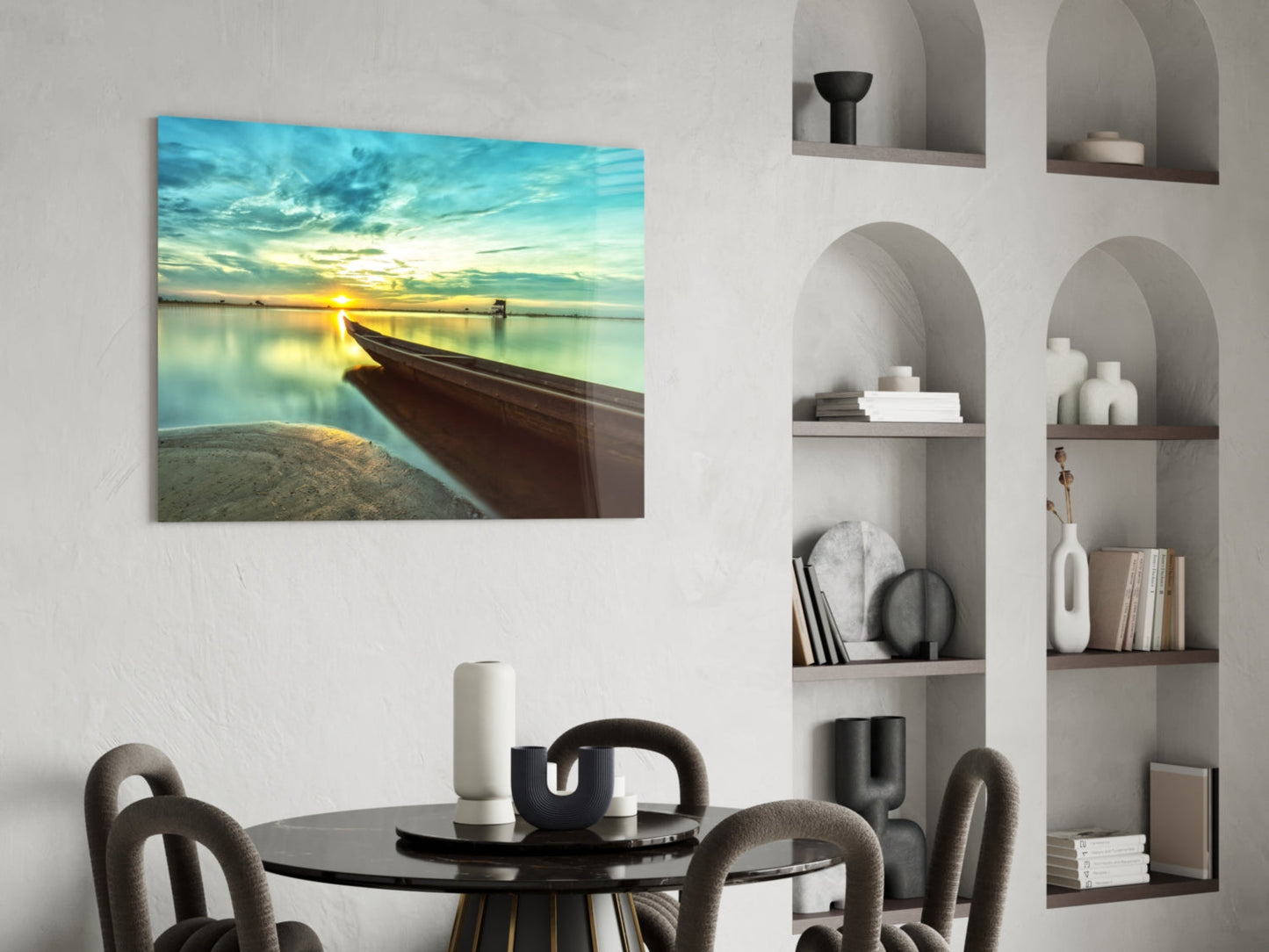 Glass wall art print displayed above a black round dining table showing a wooden kayak beached at sunset with turquoise water and golden sky.