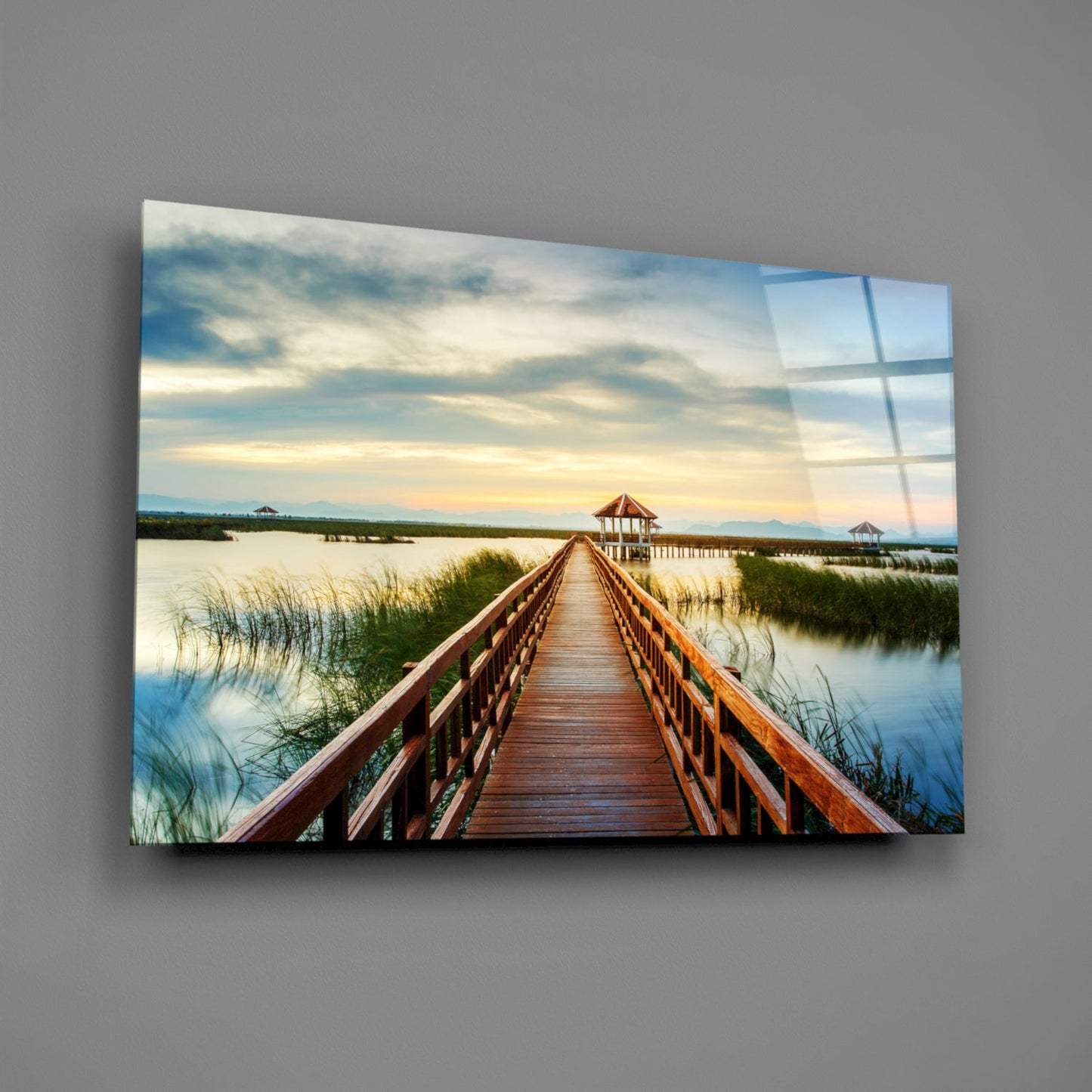 Wooden boardwalk stretching toward distant gazebos across calm marshland waters at sunset, displayed as framed glass wall art.