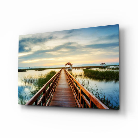 Wooden boardwalk extending toward a gazebo across calm water with marsh grasses, cloudy sky at sunset.