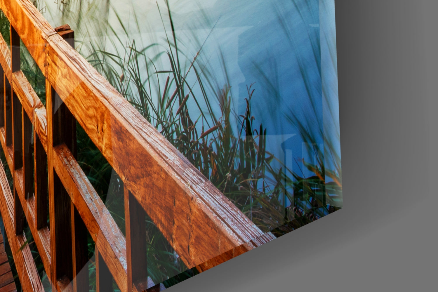 Glass wall art panel displaying wooden dock railing and marsh grasses with blue water reflection.