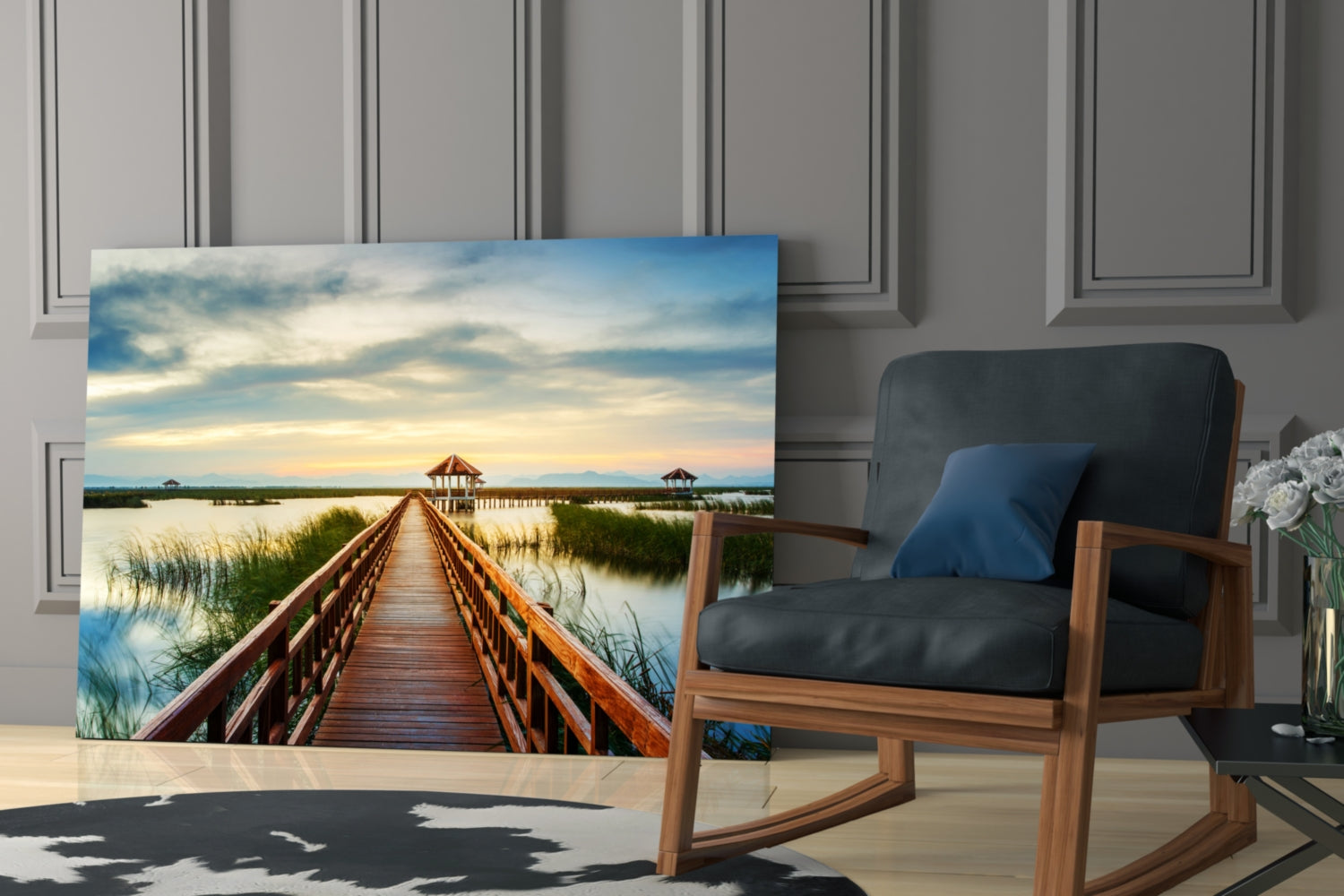Glass wall art depicting a wooden boardwalk stretching toward distant pavilions across a wetland landscape at sunset, displayed in a modern living room setting.