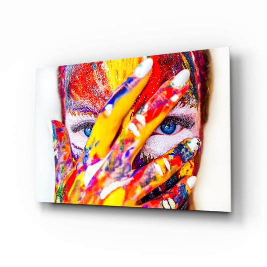Person's face and hands covered in multicolored paint and pencils, displayed as glass wall art against white background.