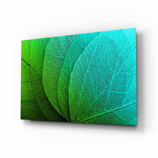 Angled perspective view of glass wall art displaying overlapping leaf veins transitioning from bright lime green on the left to turquoise on the right.