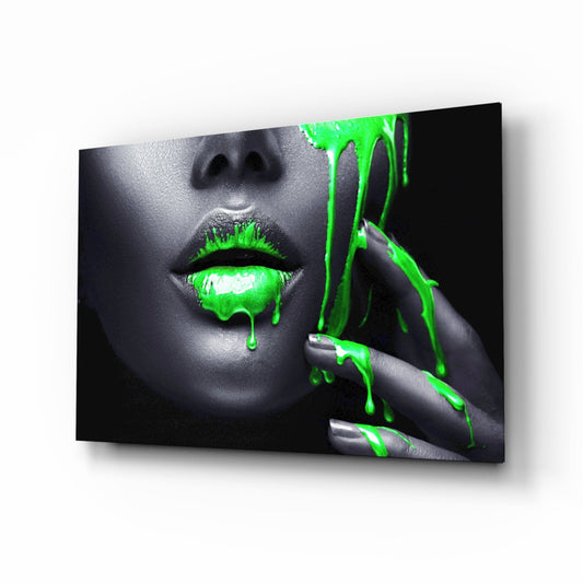 Angled product view of glass wall art featuring a grayscale face with neon green paint dripping from lips and hand against black background.