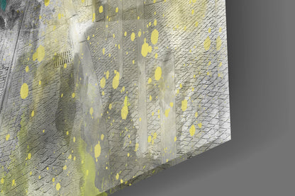 Close-up angled view of textured brick wall with yellow paint splatters and vertical concrete dividers against gray background.