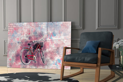 Glass wall art featuring a red bicycle against a pink and blue watercolor brick background, displayed in a modern living room next to a wooden chair.