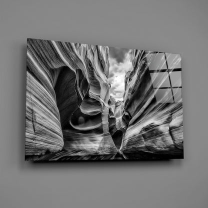Black and white glass wall art depicting a narrow slot canyon with striated rock walls framing a sky opening above.