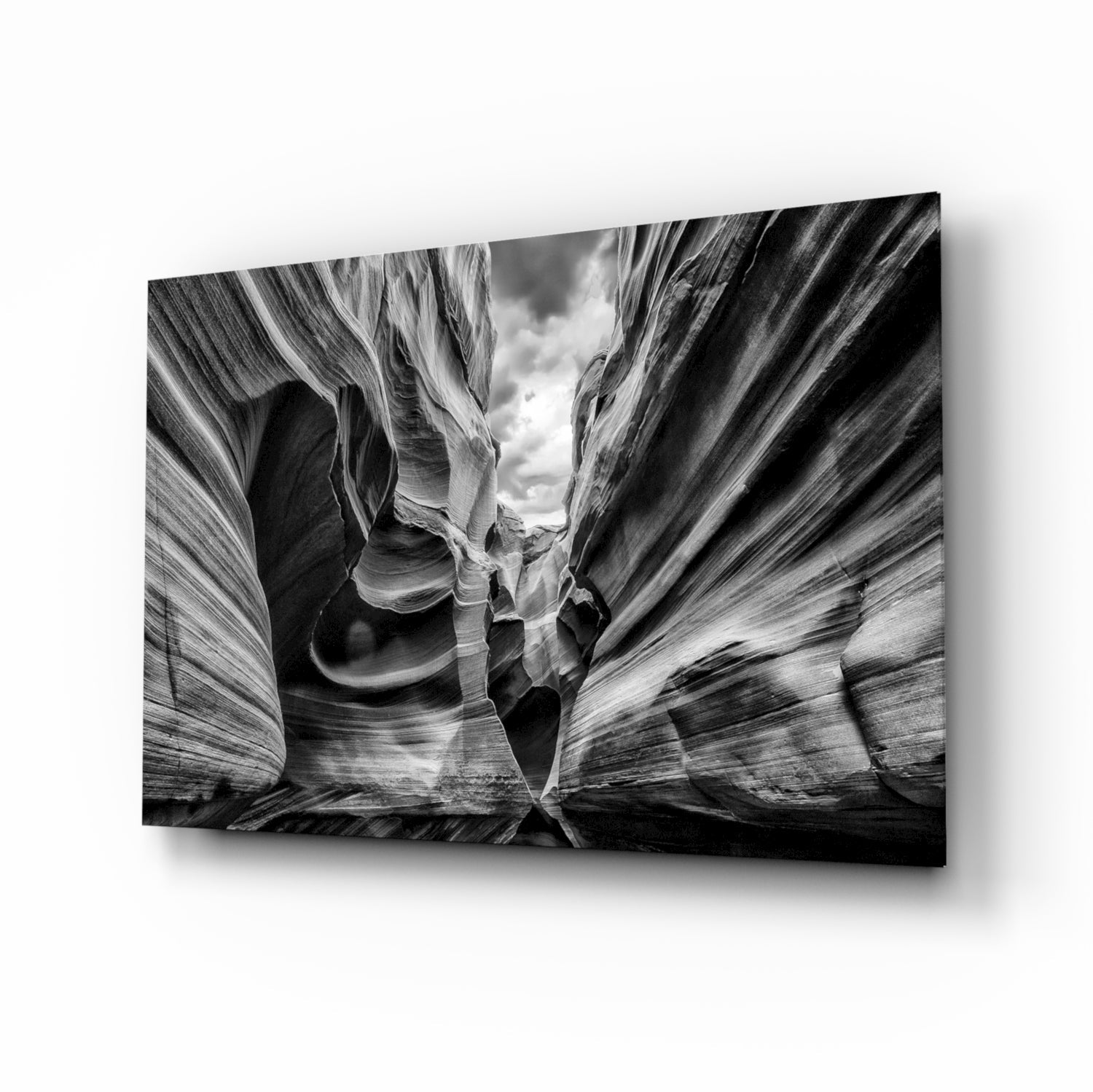 Black and white glass wall art displaying a dramatic upward view through a narrow canyon with layered rock walls and sky visible at the top.