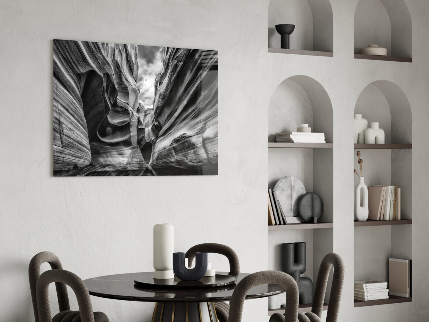 Black and white glass wall art depicting layered canyon rock formations displayed above a round dining table with curved chairs and built-in shelving.