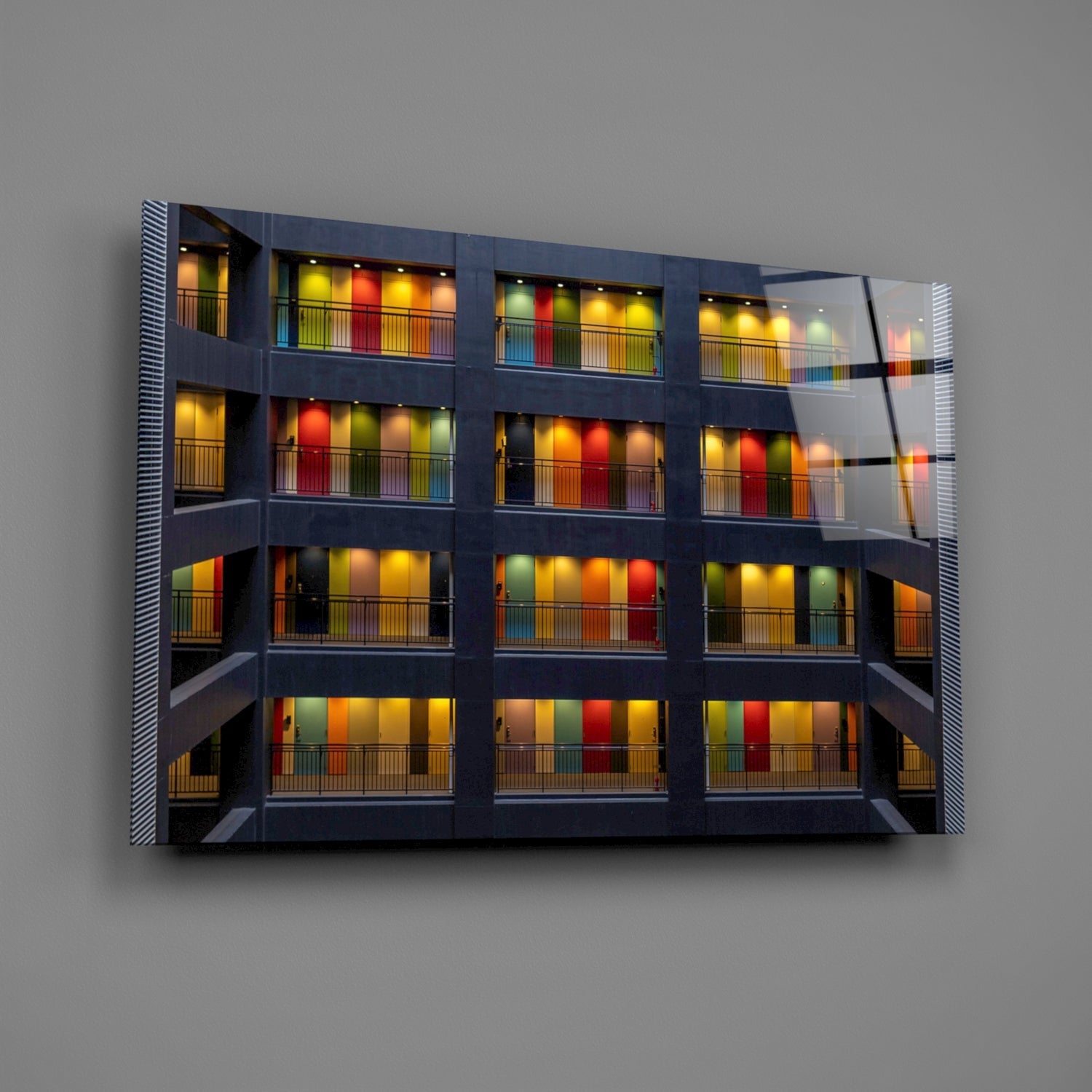 Modern glass wall art featuring a multi-story building facade with colorful illuminated window panels in red, yellow, green, and orange against dark framework.