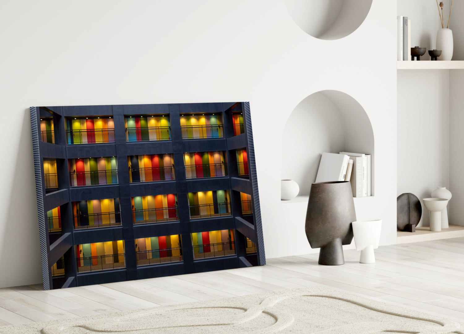 Framed glass wall art leaning against white wall displays illuminated building facade with colorful books on shelves behind grid windows.