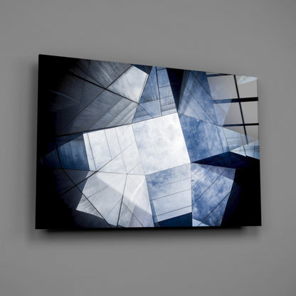 Abstract geometric glass wall art with overlapping translucent blue and white panels against dark background, mounted on gray wall.
