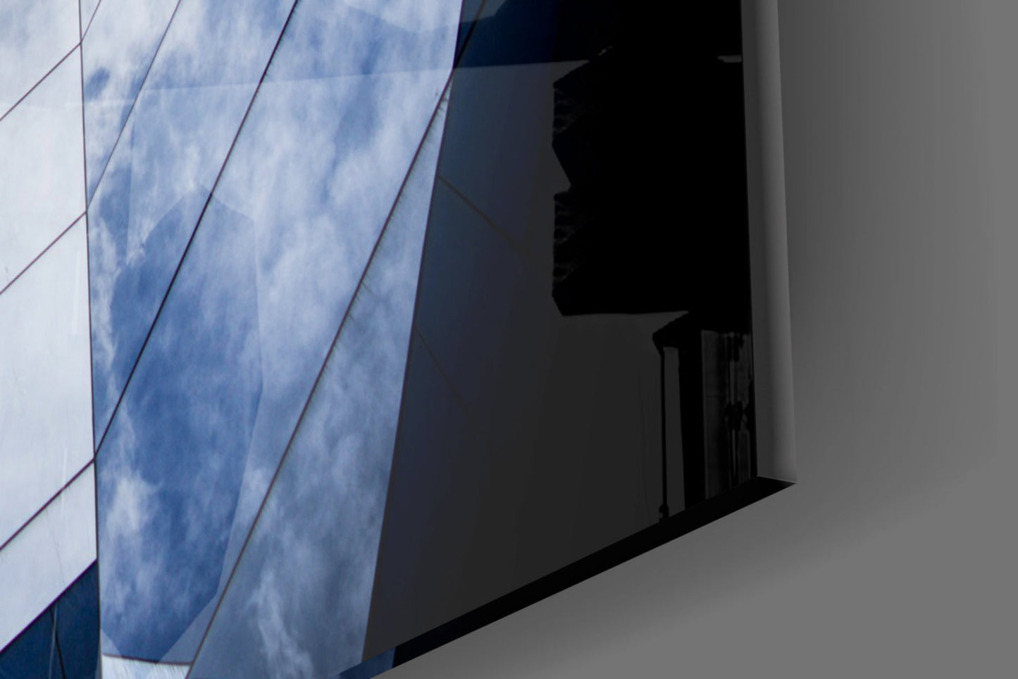 Modern glass wall with blue cloud reflections and geometric diagonal lines casting shadows on white surface.