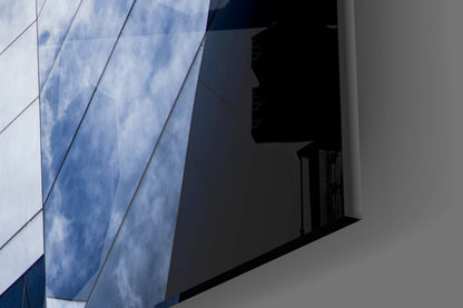 Modern glass wall with blue cloud reflections and geometric diagonal lines casting shadows on white surface.