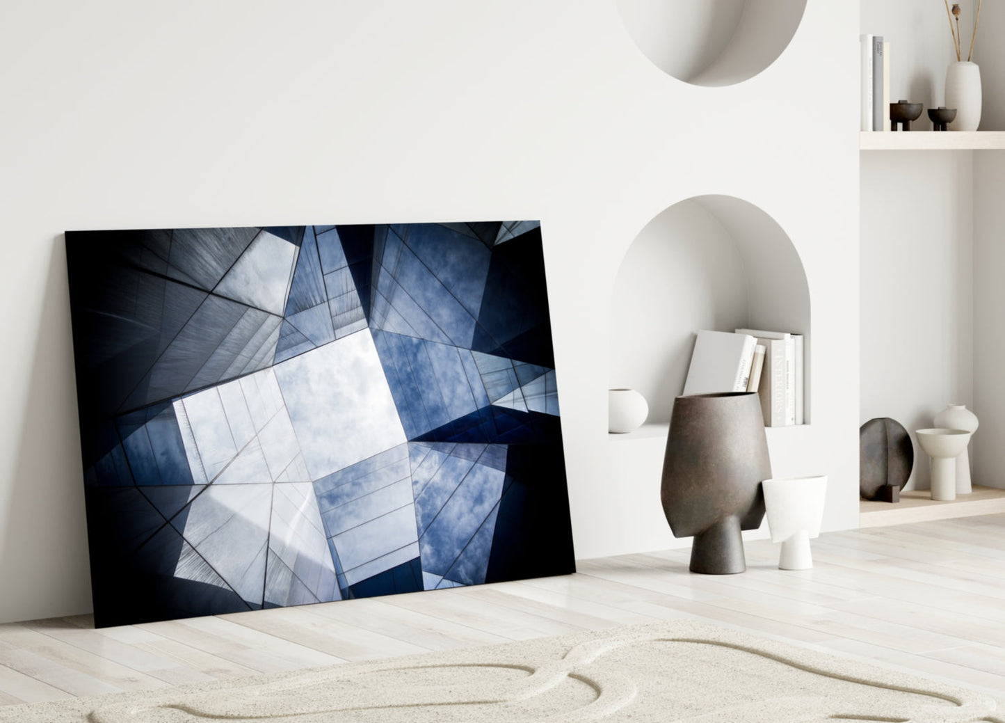 Modern geometric glass wall art with blue and white angular architectural patterns leaning against white wall in minimalist interior.