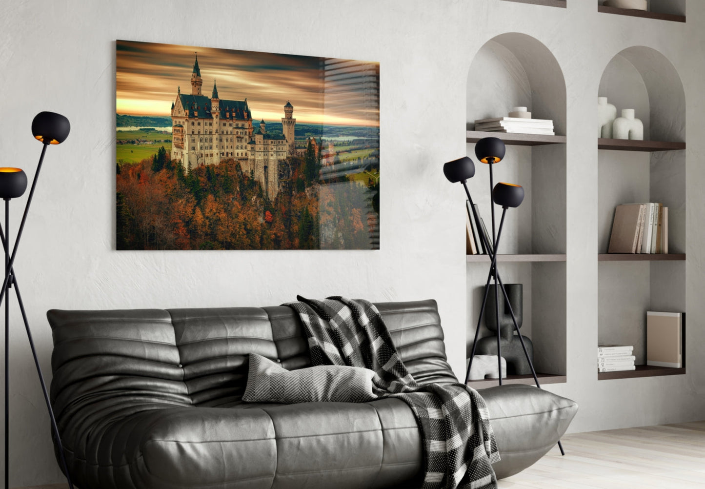 Castle glass wall art displaying Neuschwanstein Castle at sunset, hung above a black leather sofa in a modern living room.