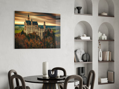 Castle glass wall art displaying Neuschwanstein Castle at sunset, mounted above a dining table in a modern interior.