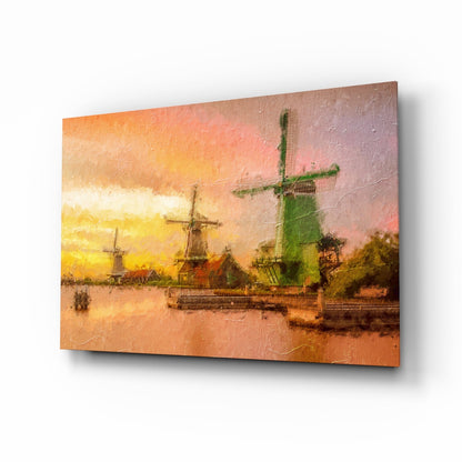 Angled view of glass wall art depicting Dutch windmills at sunset reflected in water, with warm orange and yellow tones.