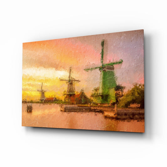 Angled view of glass wall art depicting Dutch windmills at sunset reflected in water, with warm orange and yellow tones.