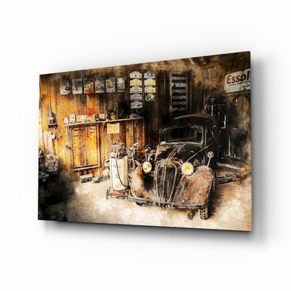 Angled product view of glass wall art depicting a vintage garage interior with rusted car, yellow gas pump, and weathered wooden walls with Esso signage.