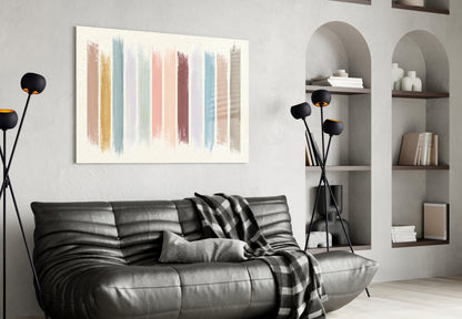 Horizontal glass wall art with vertical pastel brush strokes in muted tones displayed above a black leather sofa in a modern living room.