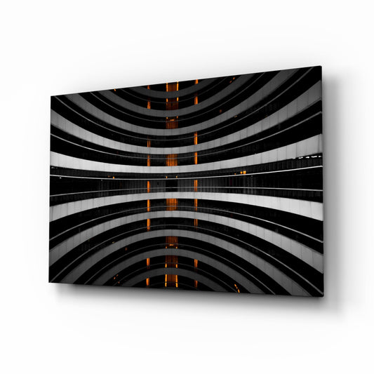 Angled view of curved black and white striped glass wall art with amber lights glowing vertically down the center.