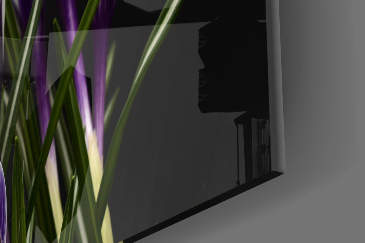 Purple flowers glass wall art displayed on gray wall with green plant foliage in foreground.