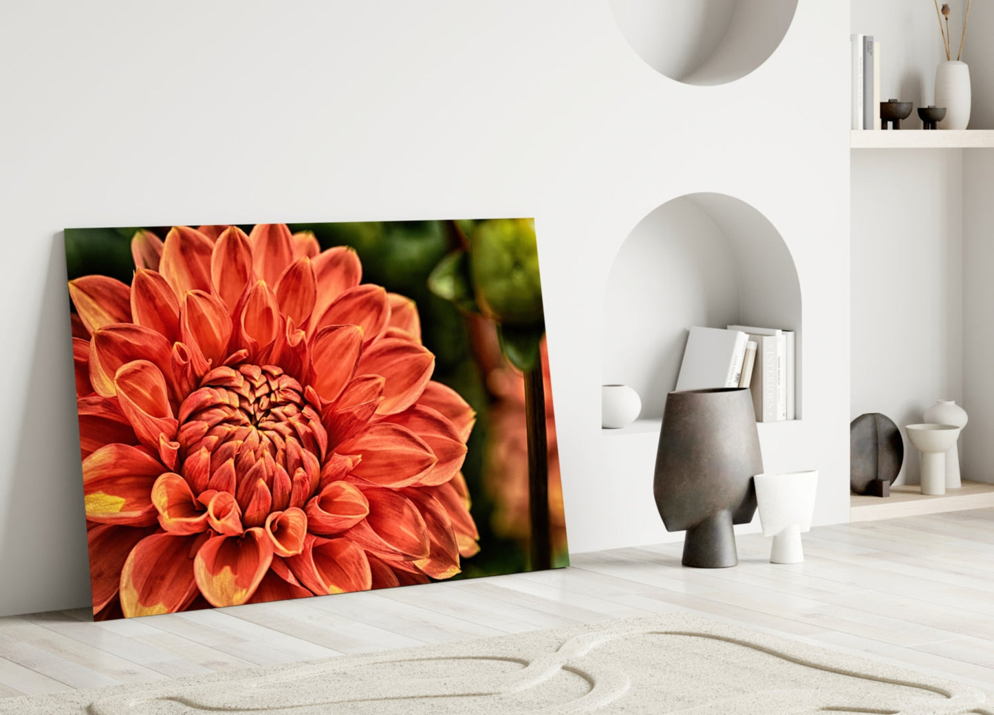 Orange Gerbera glass wall art leaning against white wall in minimalist interior with decorative objects and shelving.