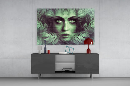 Green and black glass wall art featuring a woman's face with tropical leaves displayed above a dark media console in a modern living room setting.