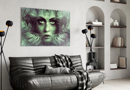 Glass wall art depicting a woman's face with green-tinted tropical leaves, displayed above a black leather sofa in a modern living room.