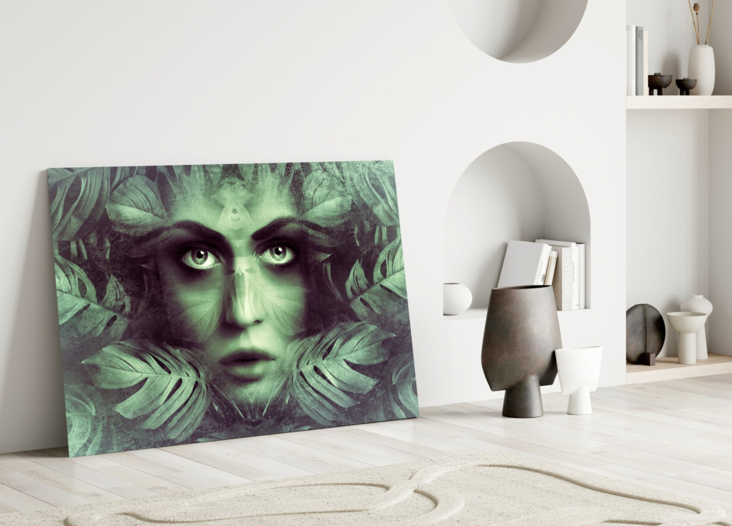 Glass wall art leaning against white wall displays green-toned woman's face surrounded by tropical leaf patterns in minimalist interior setting.