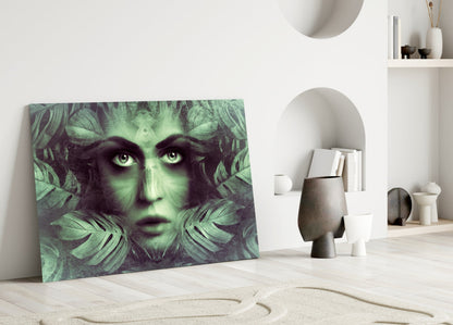 Glass wall art leaning against white wall displays green-toned woman's face surrounded by tropical leaf patterns in minimalist interior setting.