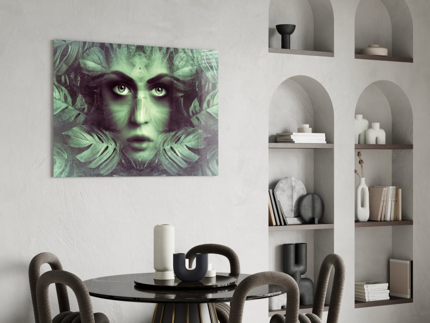 Green and black glass wall art featuring a woman's face framed by tropical leaves, displayed above a round dining table in a modern interior.