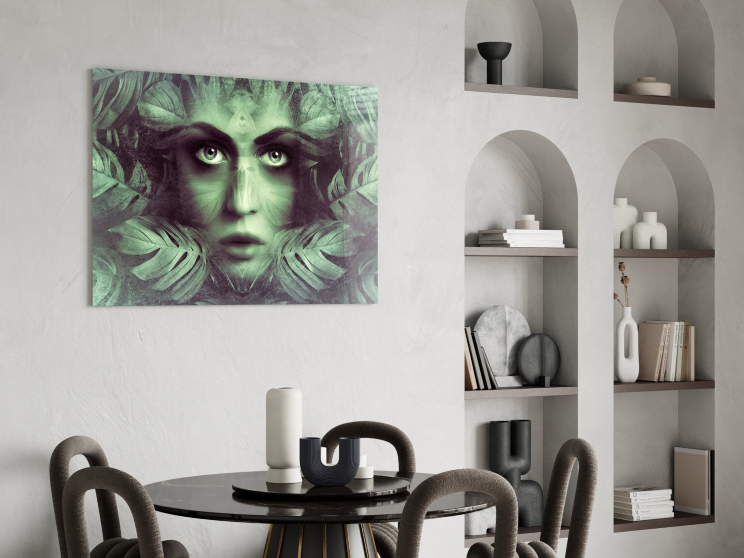 Green and black glass wall art featuring a woman's face framed by tropical leaves, displayed above a round dining table in a modern interior.