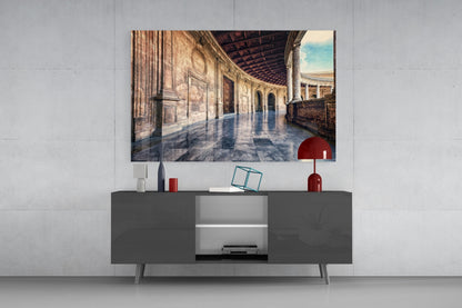 Baroque Building Glass Wall Art depicting a sunlit classical colonnade displayed above a dark gray media console with red decorative accessories.