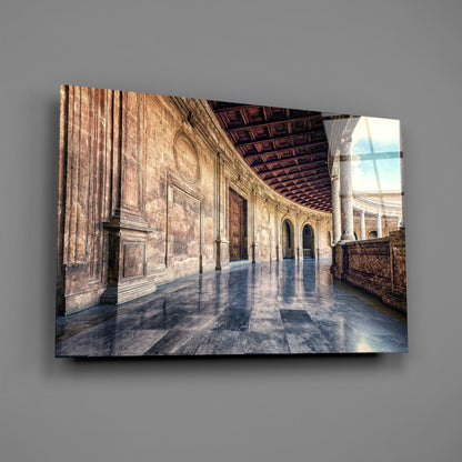 Glass wall art depicting a sunlit baroque colonnade with stone arches, wooden ceiling, and reflective floor against gray wall.